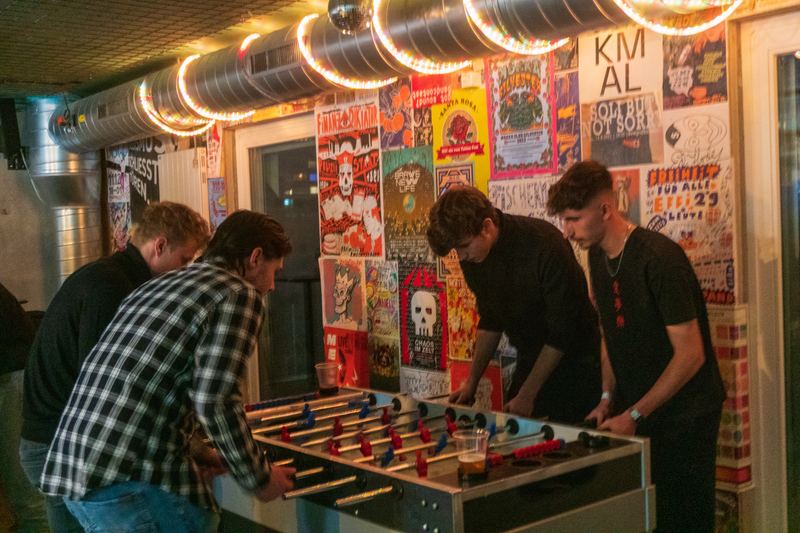 Guests playing table football in a venue with string lights and a wall covered in posters.