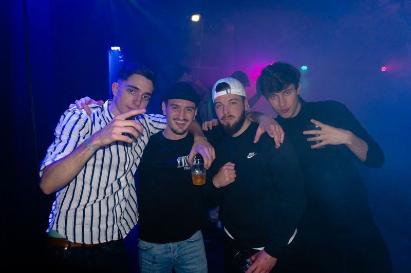 Four friends celebrating together in a club bathed in blue and magenta light.