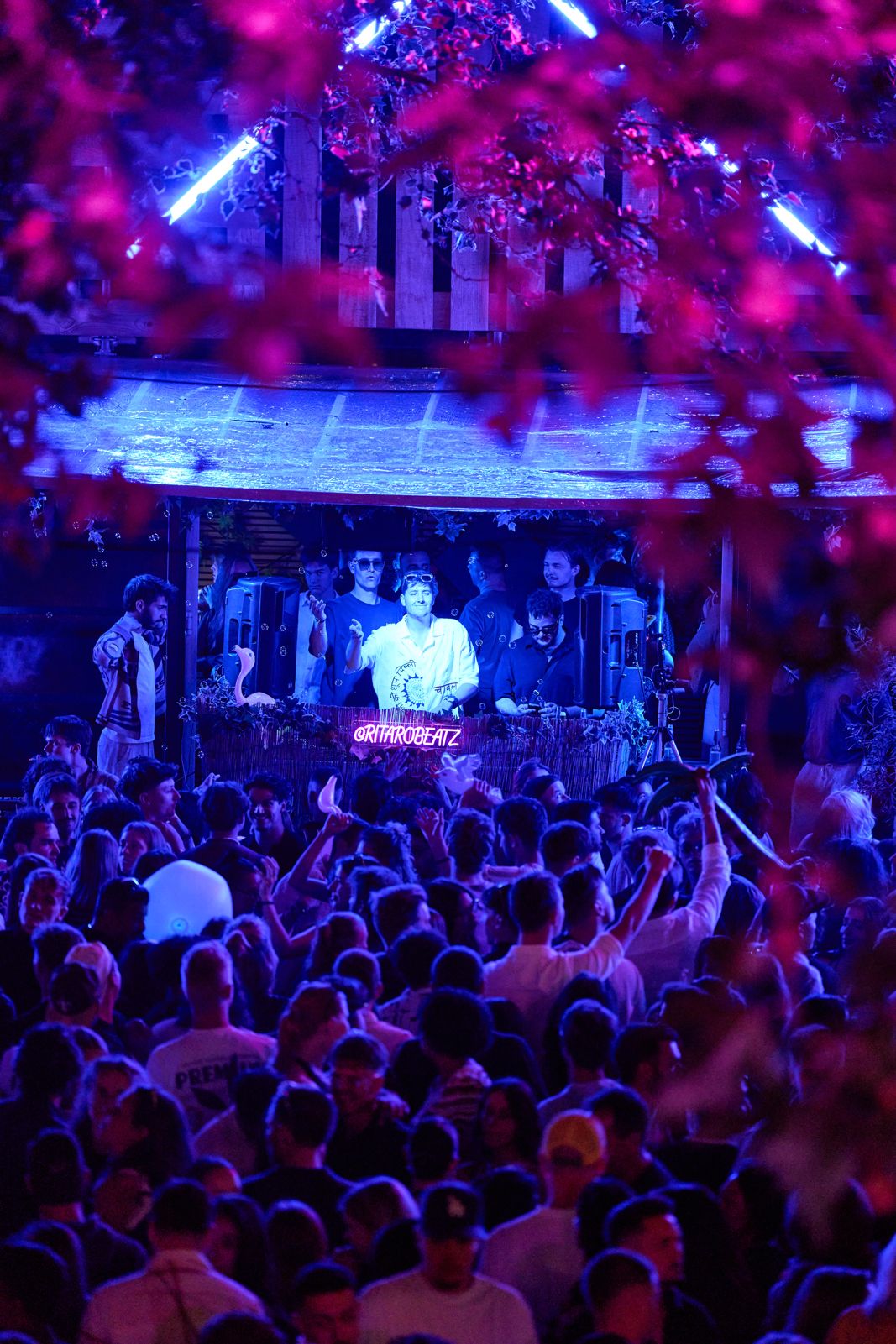 DJ Ritaro on stage behind the decks, facing a packed crowd under pink and blue lights.